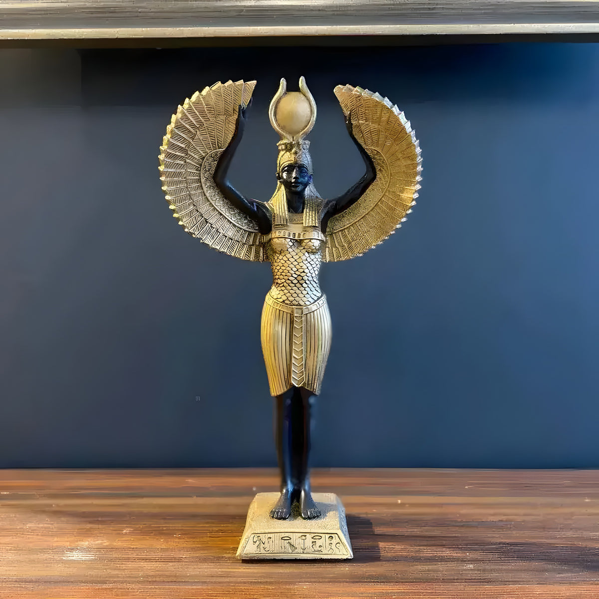 Egyptian Goddess Isis sculpture, full front view, black body, gold feathered wings spread, arms raised holding orb, inscribed base