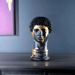 Matte black Hermes bust with gold gilding brushstrokes on face and collar, front view on dark console