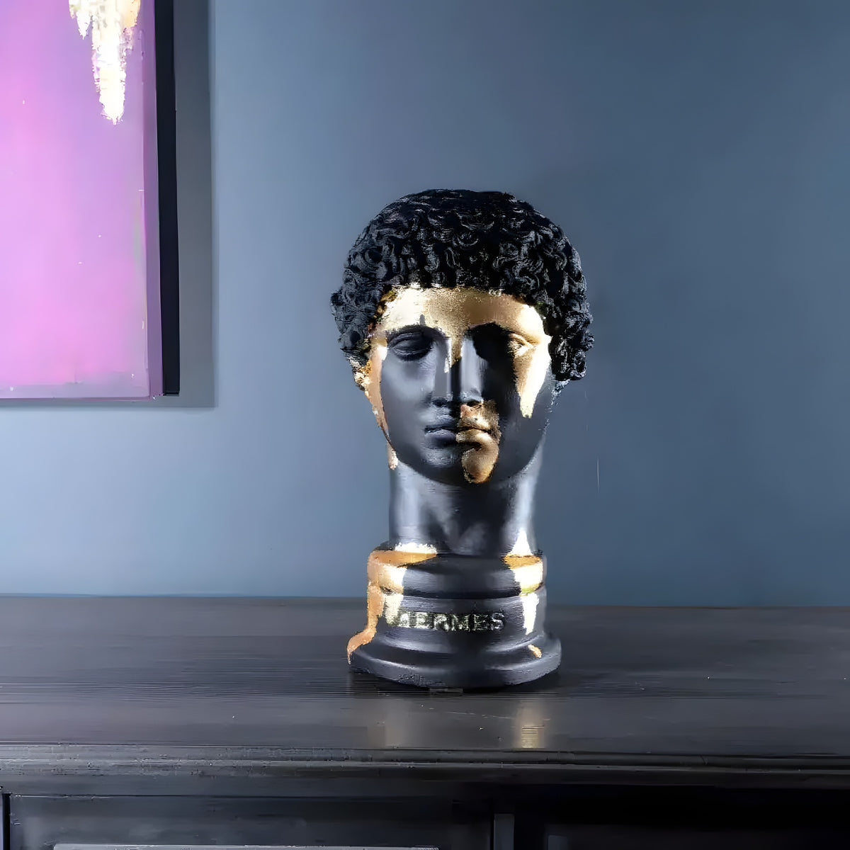 Matte black Hermes bust with gold gilding brushstrokes on face and collar, front view on dark console