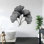 Black ginkgo leaf metal wall hanging in a modern bathroom above freestanding tub with plant