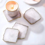 Four white quartz agate coasters with jagged gold edges arranged around a lit tealight candle