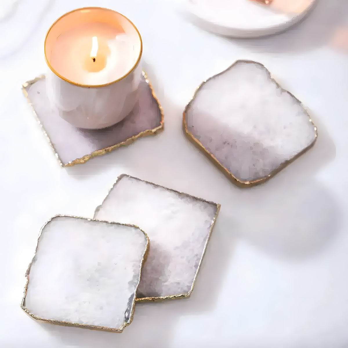 Four white quartz agate coasters with jagged gold edges arranged around a lit tealight candle