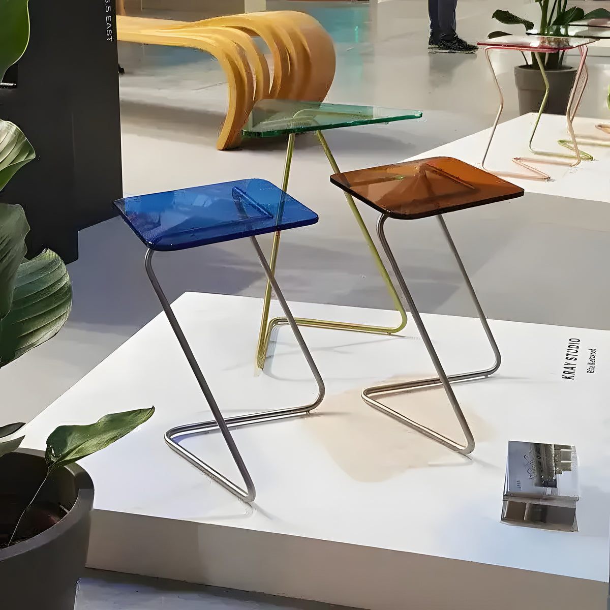 Blue and amber Diamond Crystal Tables on metal zigzag frames displayed at design exhibition with plants