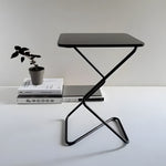 Black square side table with zigzag metal frame, styled next to stacked books and small potted plant on white surface