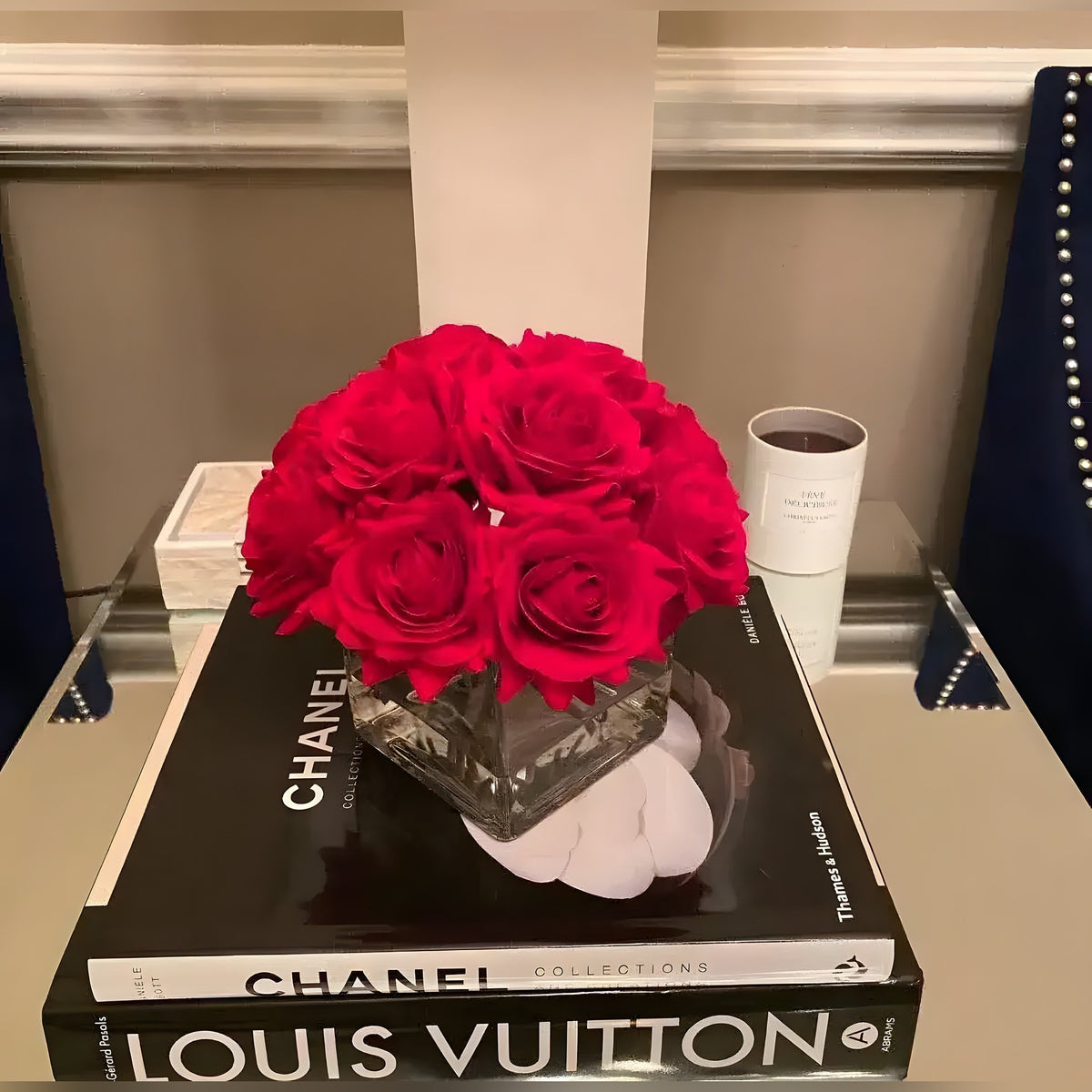 Faux red silk rose centerpiece in a square glass vase placed atop fashion coffee table books in a styled vignette