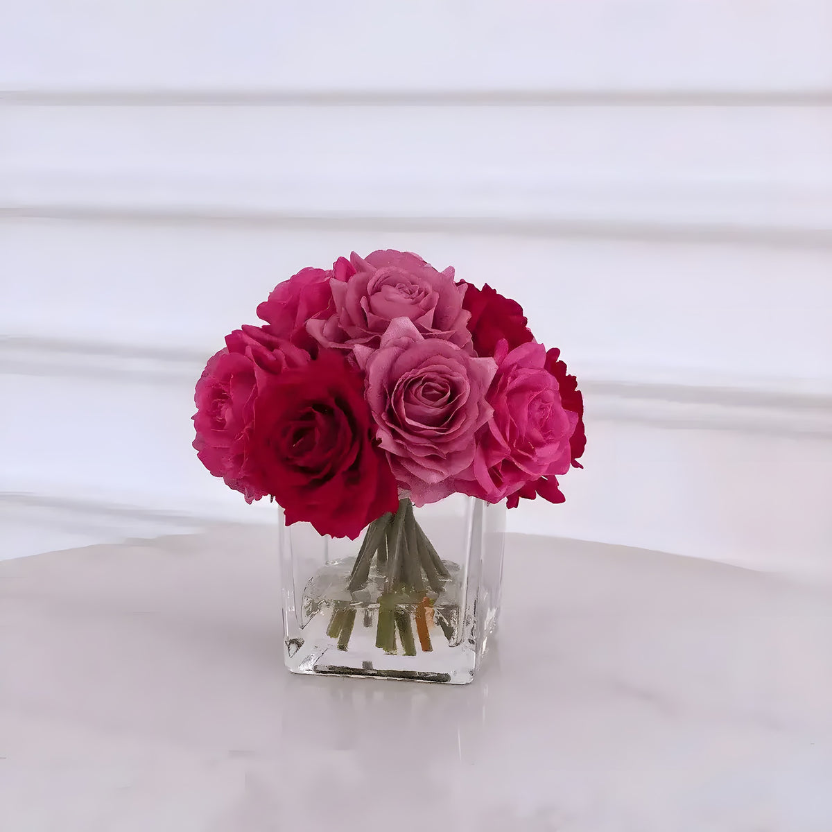 Mixed pink and red artificial silk rose centerpiece in square clear glass vase with acrylic water