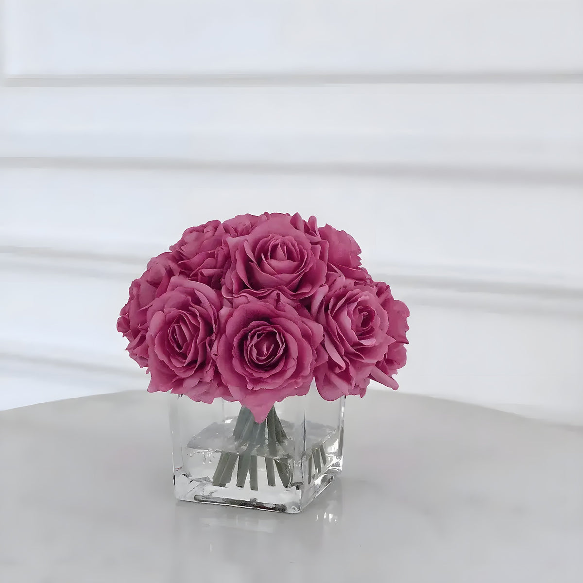 Mauve purple silk rose centerpiece in a square glass vase with simulated water on marble surface
