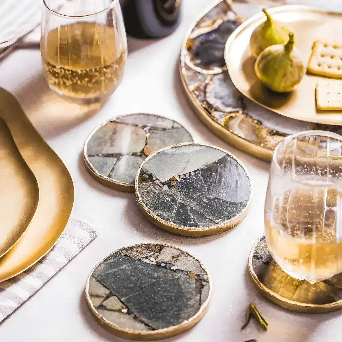 Four round green aventurine agate coasters with gold trim styled on white table with wine glasses and figs