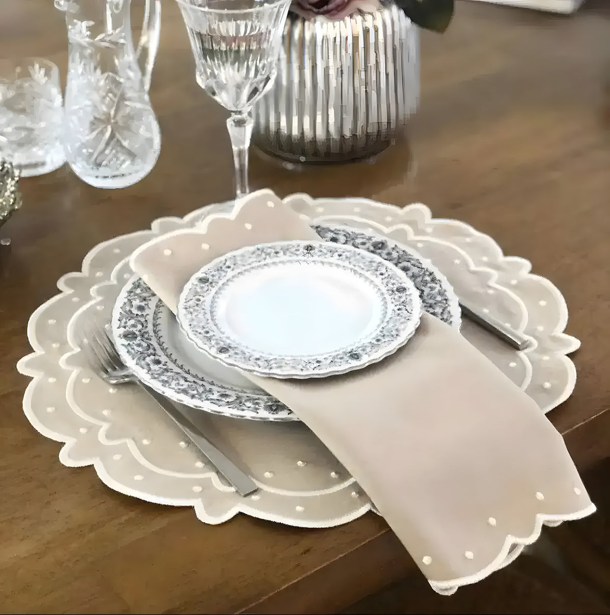 Beige scalloped cotton placemat with white embroidered edge and matching napkin, styled with china plates on wood table