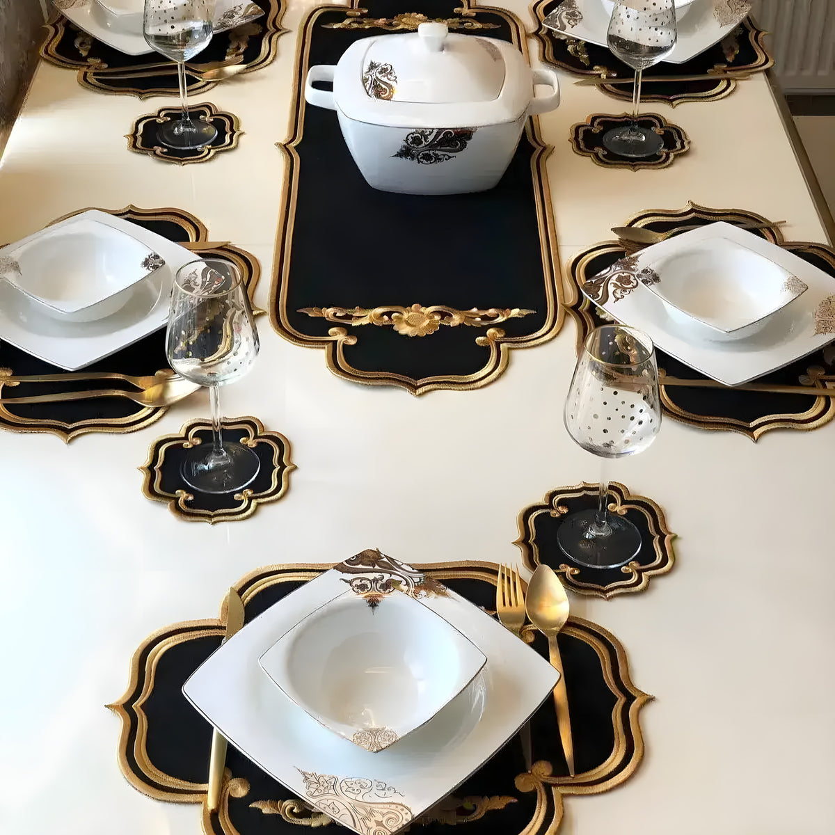 Black and gold embroidered royale table linen 13-piece set laid on a dining table with dishes and wine glasses