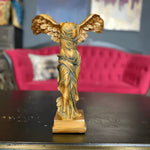 Gold winged Victory of Samothrace sculpture on dark table, red velvet sofa background