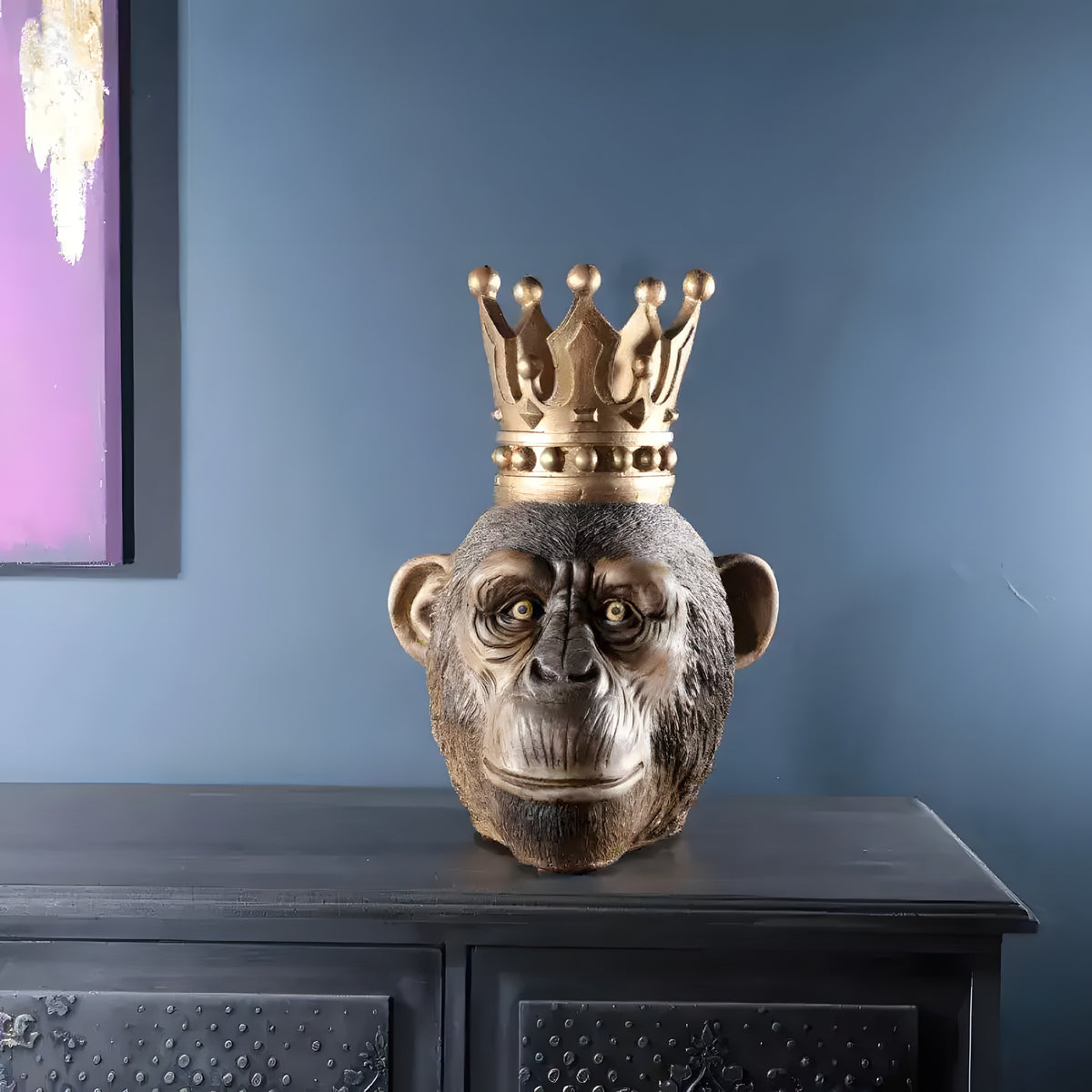 Bronze-toned resin monkey king bust with gold crown on dark sideboard against blue-gray wall