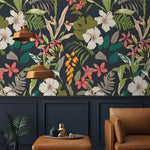 Tropical wallpaper with bright pink, coral, and white florals and green palm leaves on a dark navy background in a living room setting.