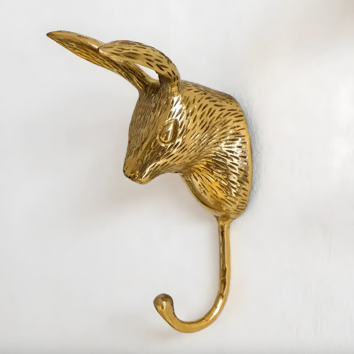 Single brass rabbit head wall hook, textured fur, upright ear, polished gold finish, curved hook below, close-up