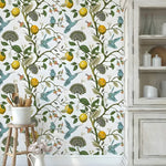 Vintage hummingbird wallpaper with blue hummingbirds, lemons, and green tree branches on white, installed behind a wood stool and rustic cabinet