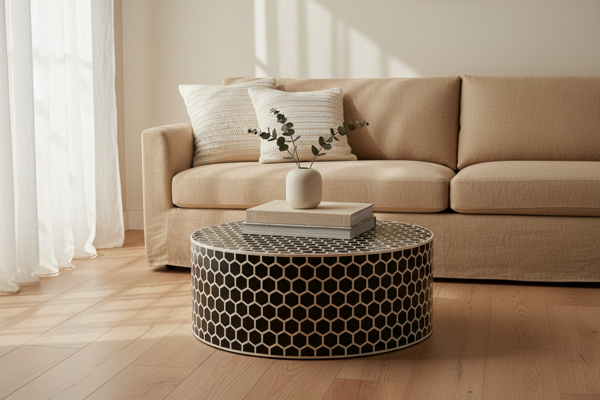 A beige fabric sofa in a bright living room with a round black-and-white honeycomb patterned coffee table, white pillows, and a small vase on top.