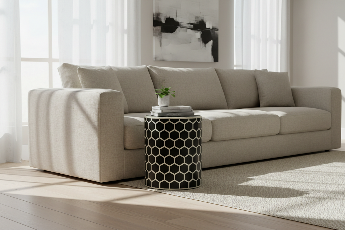 A modern beige fabric sofa in a bright, sunlit living room with a black and white geometric side table in front of it.