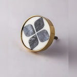 Round white marble and brass cabinet door knob with four grey marble diamond inlay pattern and gold rim, on light grey surface