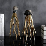 Two glam marine sculptures with dark caps and gold tentacles on black marble, grey textured backdrop