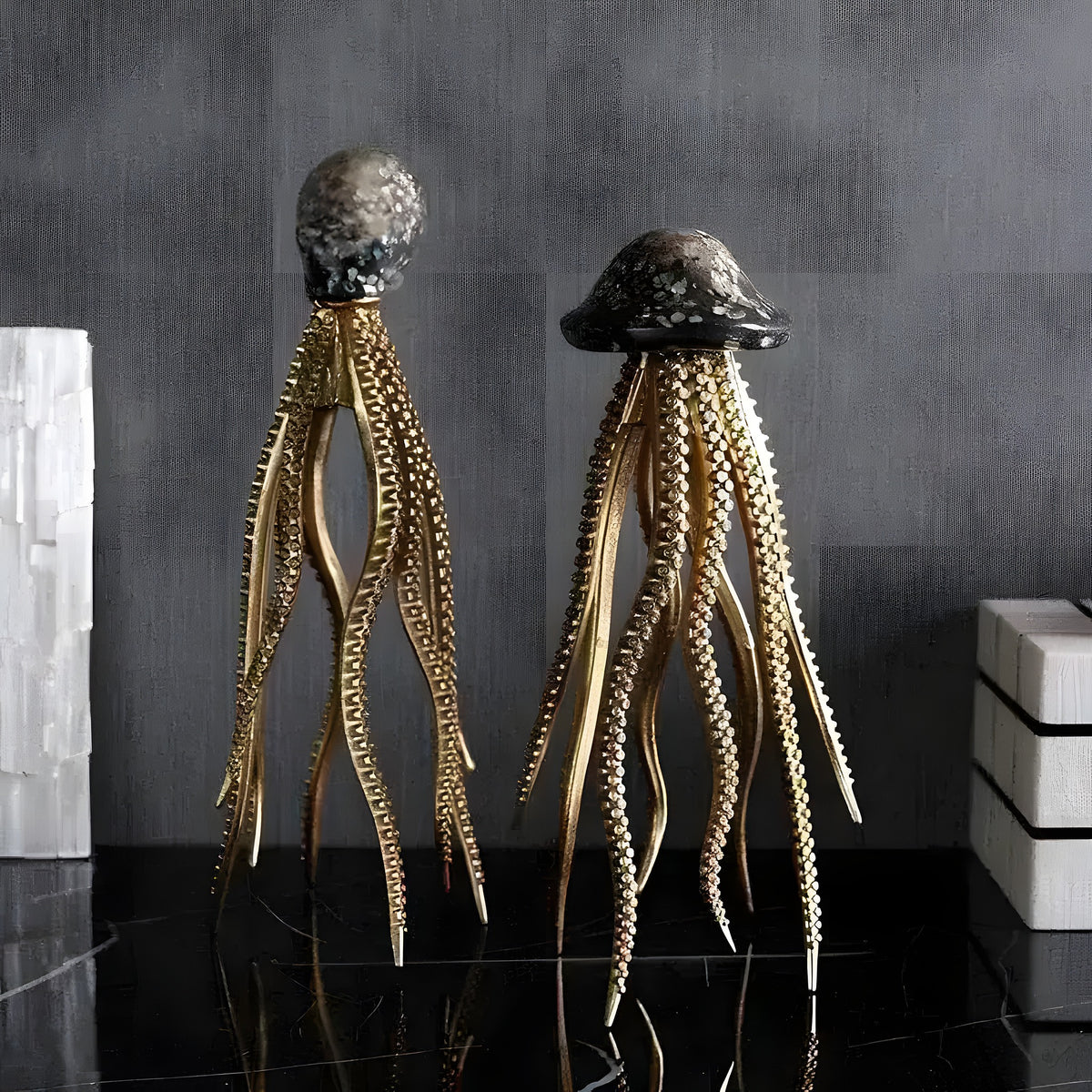 Two glam marine sculptures with dark caps and gold tentacles on black marble, grey textured backdrop