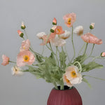 Mixed blush pink and white artificial poppy flower stems arranged in dark red ribbed vase on grey background