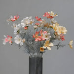Mixed pink, white, and cream daisy chrysanthemums in a dark glass vase, gray background