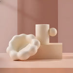 Cream coffee mug with spherical handle on cloud-shaped saucer, pink geometric backdrop
