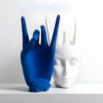 Blue matte ceramic hand and white ceramic face finger statue with spiky crown hair displayed on a white shelf
