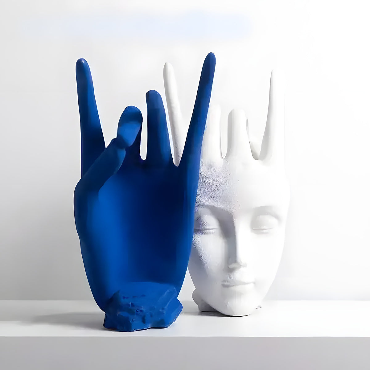 Blue matte ceramic hand and white ceramic face finger statue with spiky crown hair displayed on a white shelf
