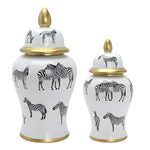 Two zebra ceramic ginger jars in large and small sizes, white with black zebra print and gold trim, gold finial lids