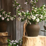 Silk thyme flower branch with white-lilac blossoms and green leaves, in a rustic clay pot on wooden stump