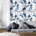 Blue and white tropical birds wallpaper with navy parrots and white hibiscus flowers, above a grey floor cushion with heart pillow