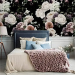 Oversized dramatic peonies on black wallpaper behind a blue velvet headboard with blue and blush pillows and a pink chunky knit throw