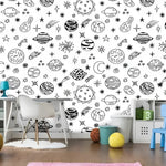 Black and white planetary celestial wallpaper in kids room with white desk and colorful toy storage