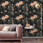 Dark tropical morning flowers wallpaper with blush hibiscus and monstera leaves, styled with a pink velvet sofa and gold floor lamp