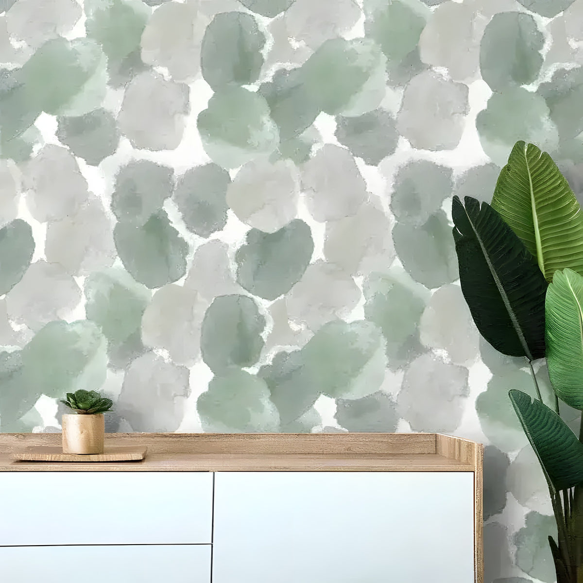 Abstract moss green watercolor wallpaper behind a white-wood sideboard with succulent and bird of paradise