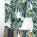Tropical oversized monstera and palm leaves wallpaper on white in bright nook with white chair and woven basket