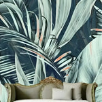 Oversized coconut and banana leaves watercolor wallpaper in blue-grey on dark navy behind ornate gold settee