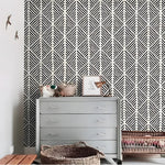 Alaia wallpaper in a nursery room setting - bold black-and-white geometric diamond stripe, gray dresser with wicker basket