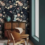 Vintage exotic flowers on dark wallpaper in a Scandi nook with a bentwood chair and antique cabinet with a teal vase