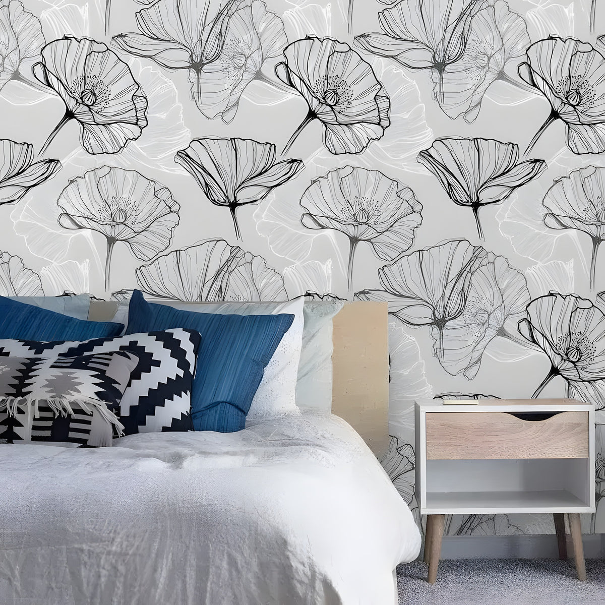 Black and white poppy floral wallpaper in a bedroom with blue denim pillows and wood nightstand