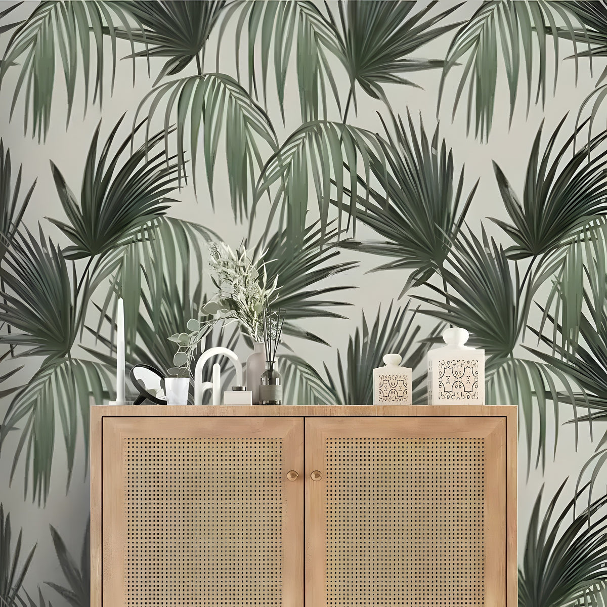 Dark green tropical palm fronds on cream vintage wallpaper; rattan sideboard with candle and vase decor below