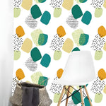 White wallpaper with scattered teal, amber and lime rounded abstract shapes beside white Eames chair and wicker basket