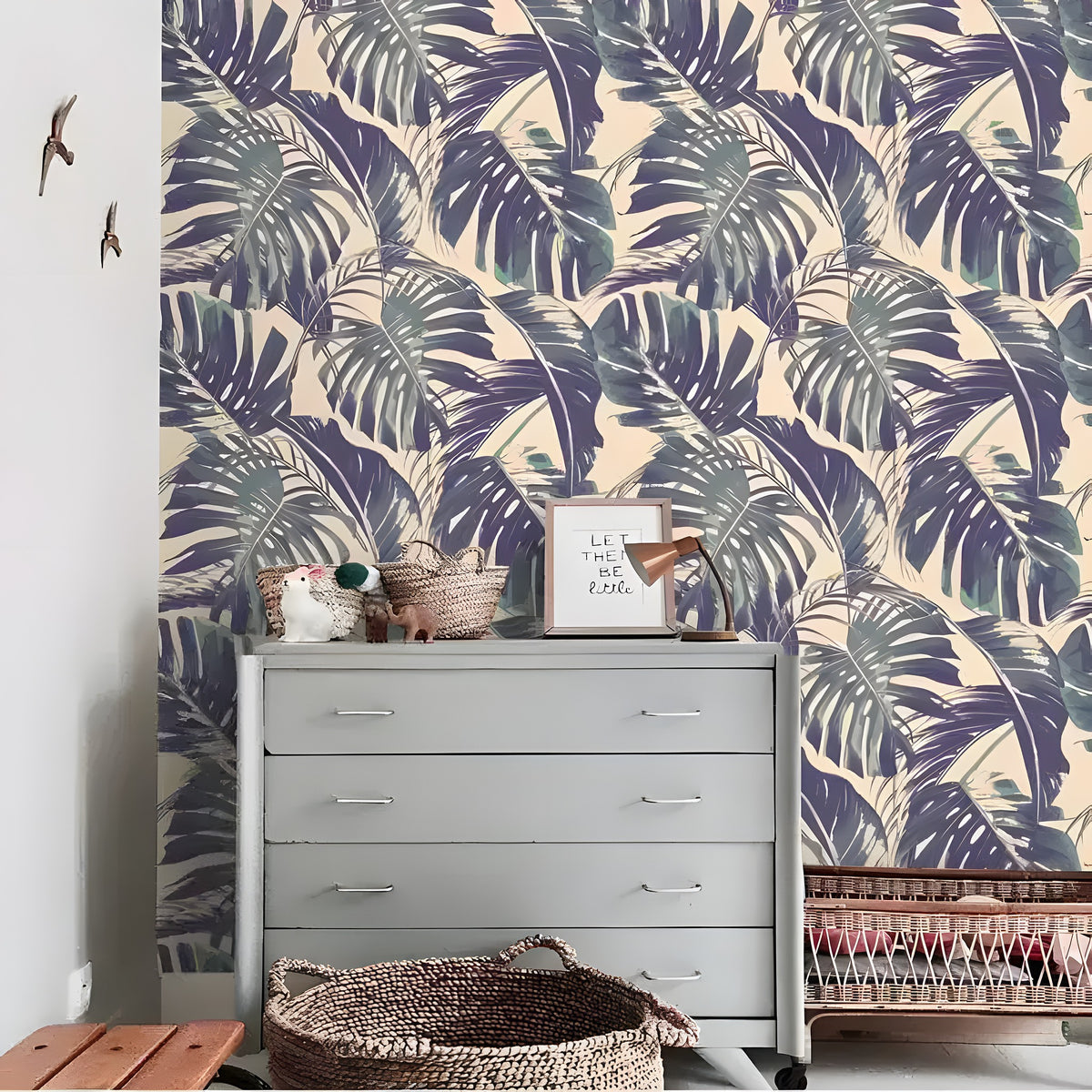 Purple and green monstera palm leaves on cream background styled on wall behind gray dresser with wicker baskets