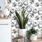 Multi-tone tropical leaves wallpaper in blue gray and gold on cream, with white armchair and rattan stool