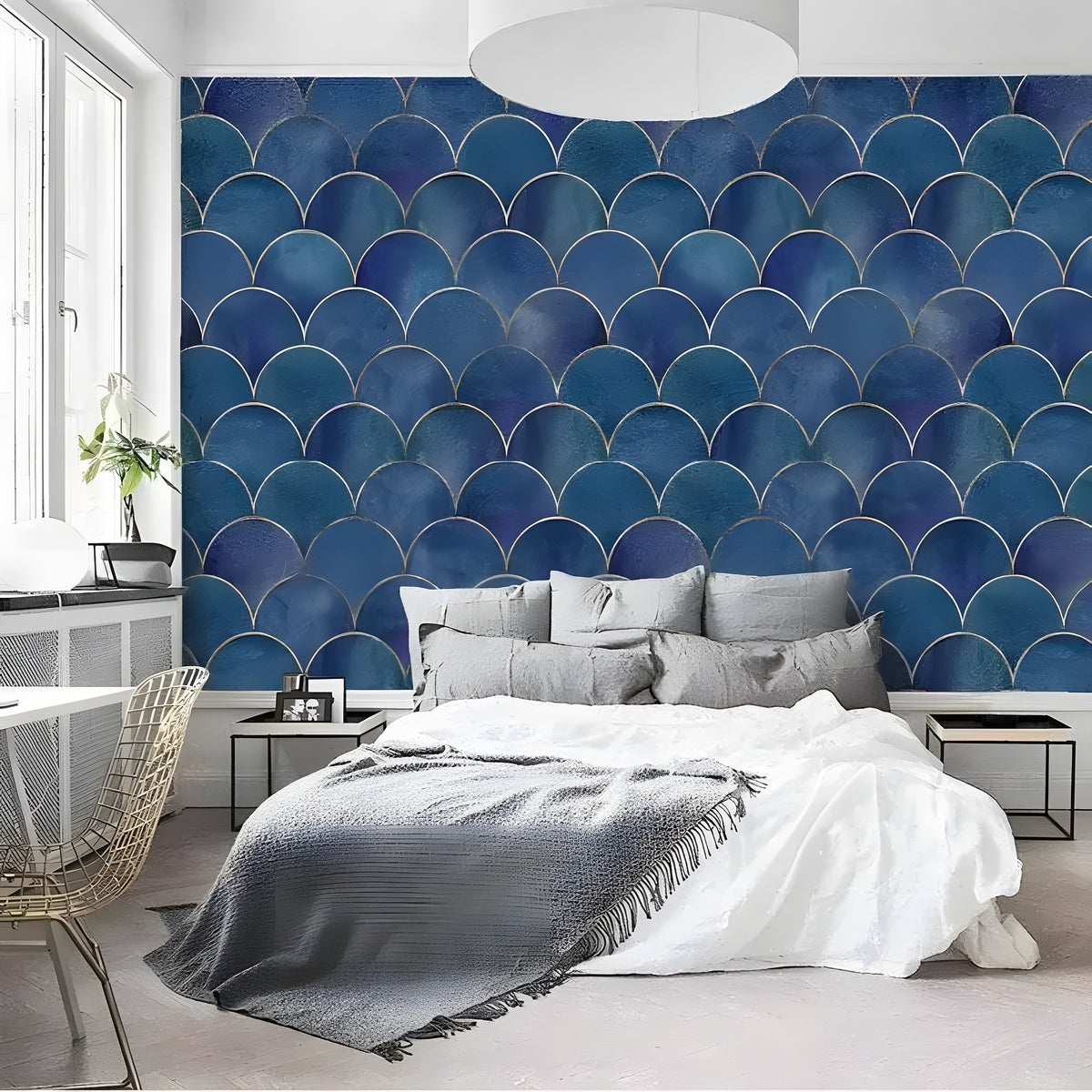 Deep navy blue fish scale art deco wallpaper as headboard wall behind white and grey bedding with gold wire chair and plant