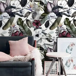 Dramatic oversized exotic floral watercolor wallpaper with burgundy hibiscus and dark leaves behind grey sofa with pink pillow
