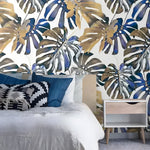 Blue oversized tropical monstera leaf wallpaper in a bright room with natural furnishings