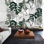 Tropical monstera leaf mural in a modern living room — dark green filled and white line-art leaves on white