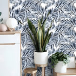 Blue tropical coconut palm leaves wallpaper in entryway with white sideboard, snake plant and wood stool
